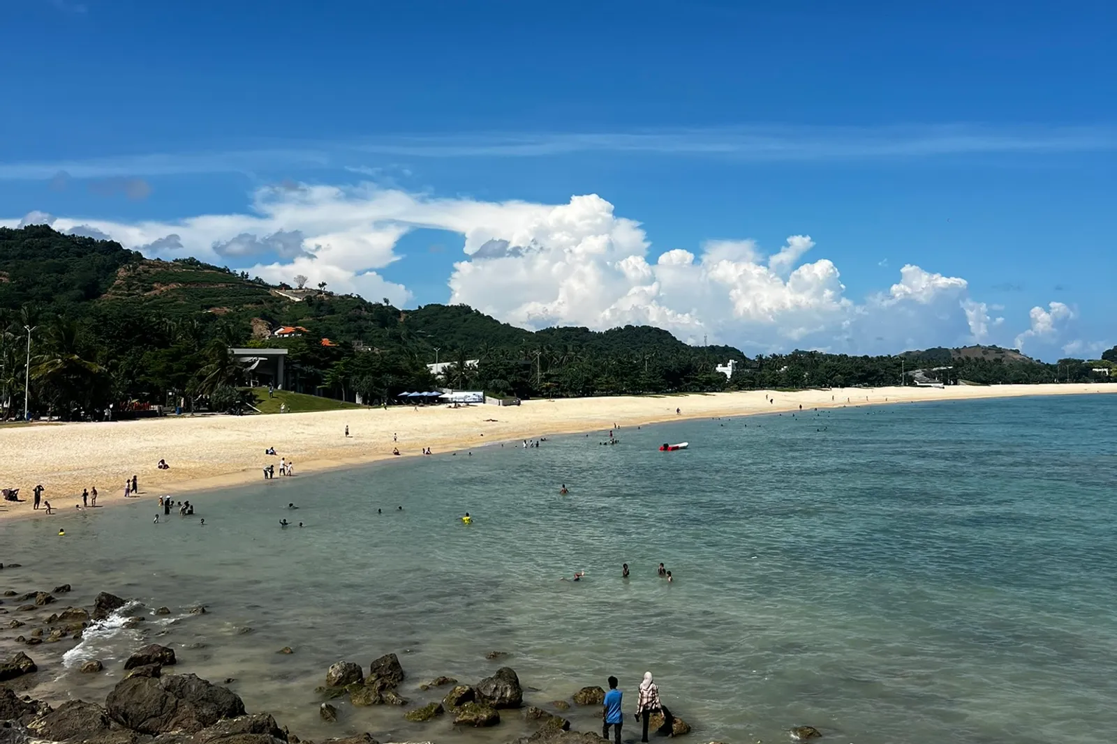The Kuta Mandalika bay, South Lombok: a long sandy beach with swimmers, headlands and hillside development.
