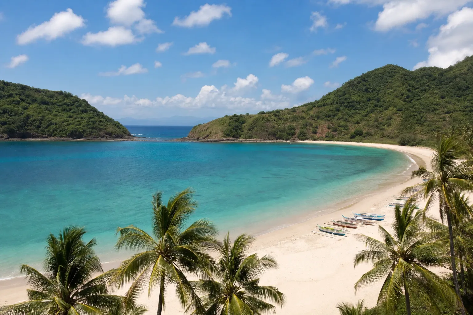 Horseshoe bay with white sand, traditional boats and green headlands in the Mawun area, South Lombok.